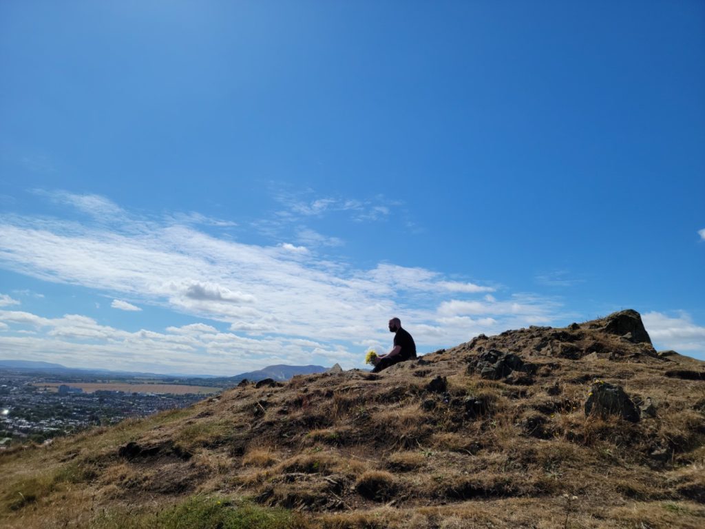 A young man holds a bouquet of yellow flowers alone at Holyrood Park