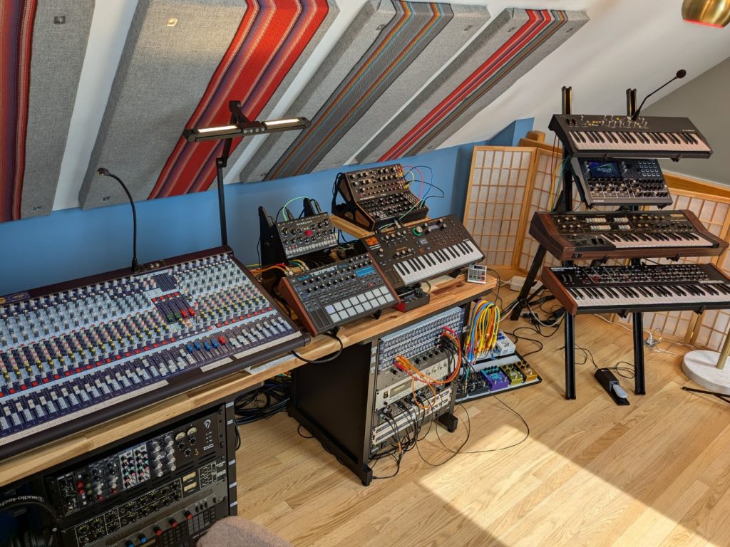 Alison Studio - 2014 An electronic music studio with light wood floors, blue walls, and acoustic panels with red striped fabric on them